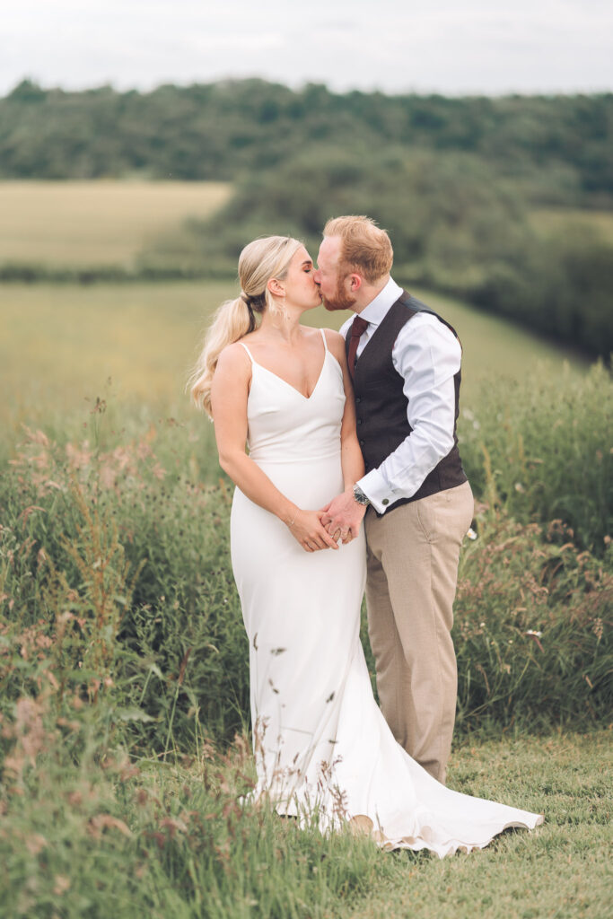 Bride and groom sharing a kiss surrounded by green fields and long grasses